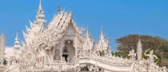 An ornate white temple with intricate spires and detailed carvings stands under a bright blue sky.