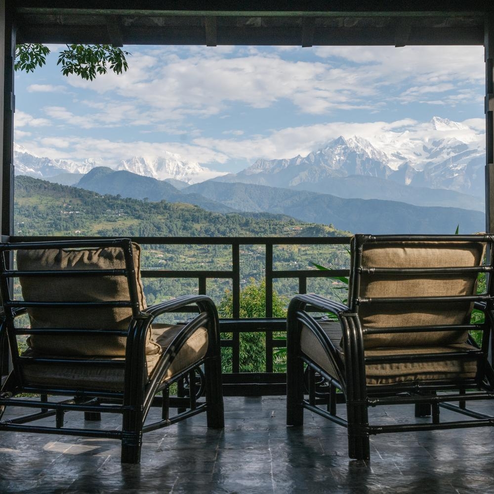 Two chairs on a balcony overlooking a panoramic mountain range.