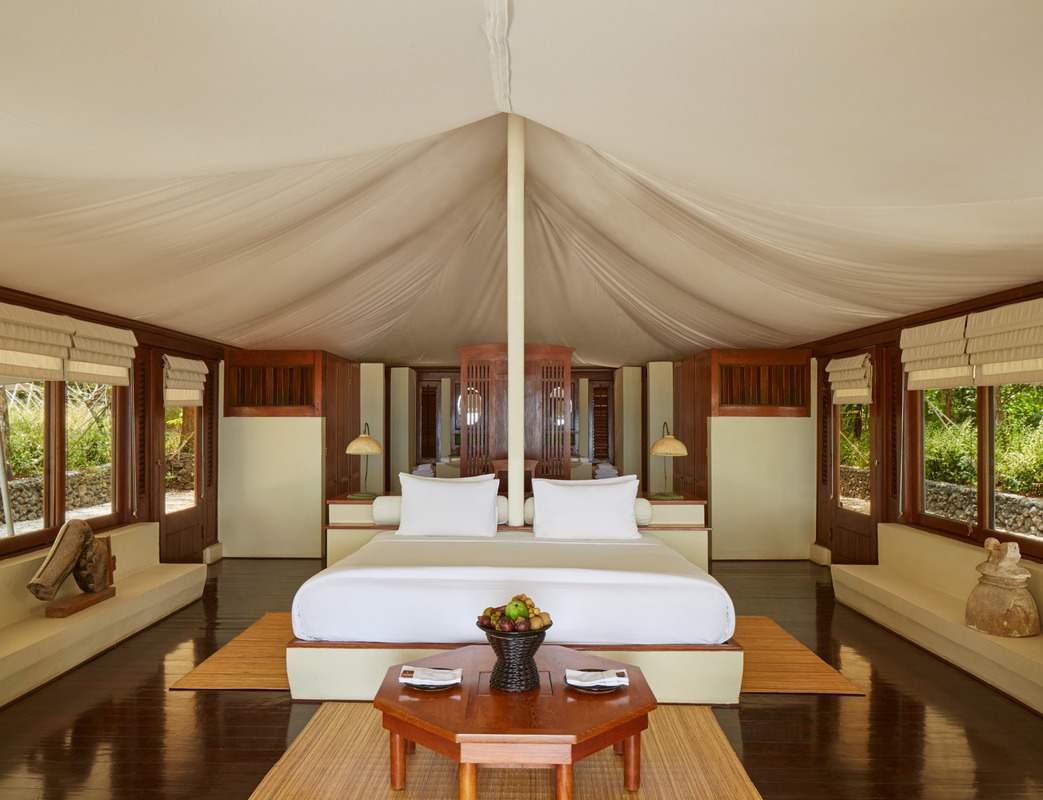Symmetrical view of a luxury tent interior at Amanwanawith a white bed, wooden accents and soft draped ceiling fabric.