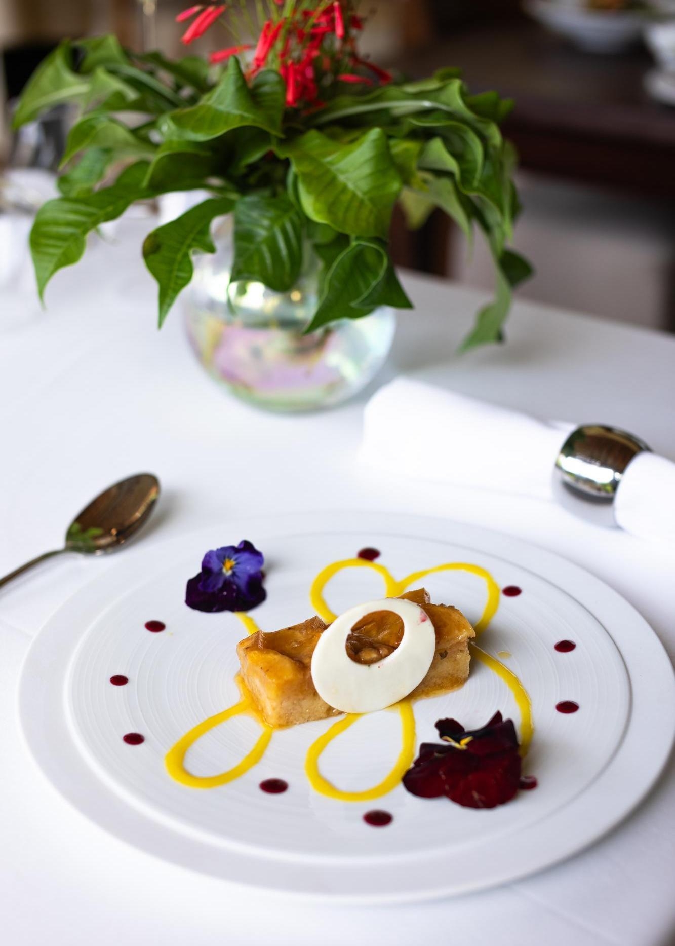 Elegant dessert plating with a pastry, cream, nut topping, and floral garnish on a white plate.