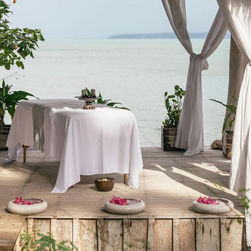 An outdoor massage table on a wooden pier overlooking the ocean with decorative flower bowls.