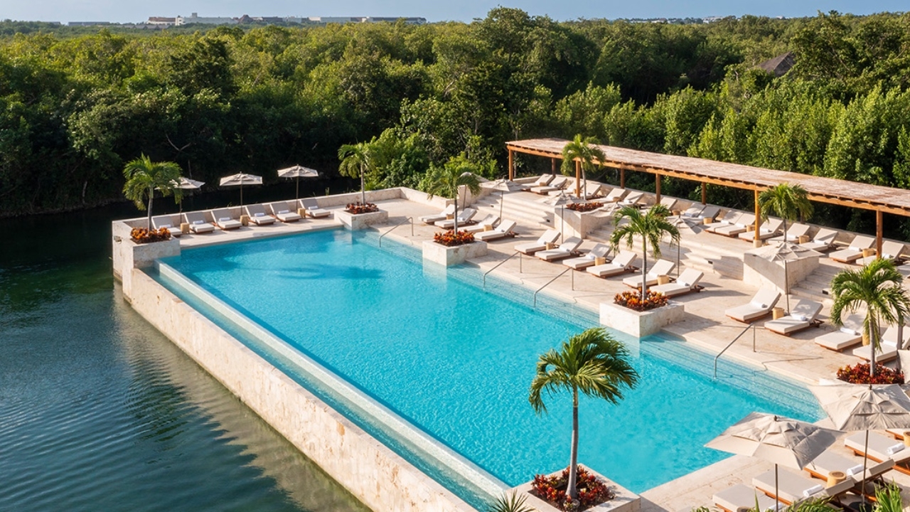 Luxury infinity pool with loungers and umbrellas overlooking lush greenery.