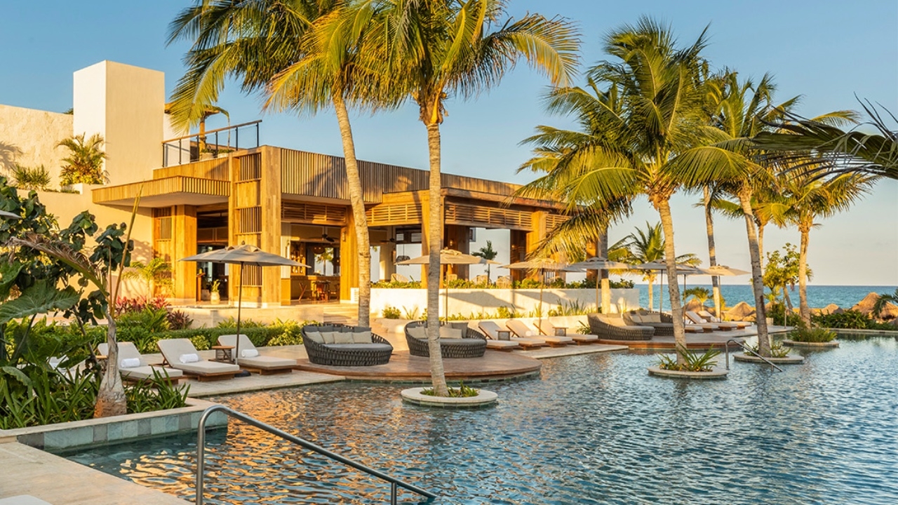 Luxury seaside resort with pool, sun loungers, umbrellas, and palm trees at sunset.