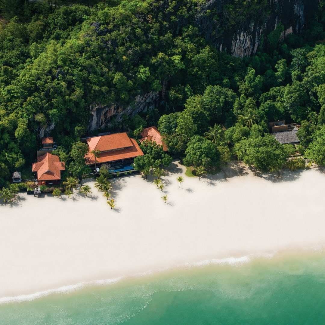 High-angle view of Four Seasons Langkawi with orange roofs tucked into a dense forest next to a white beach.