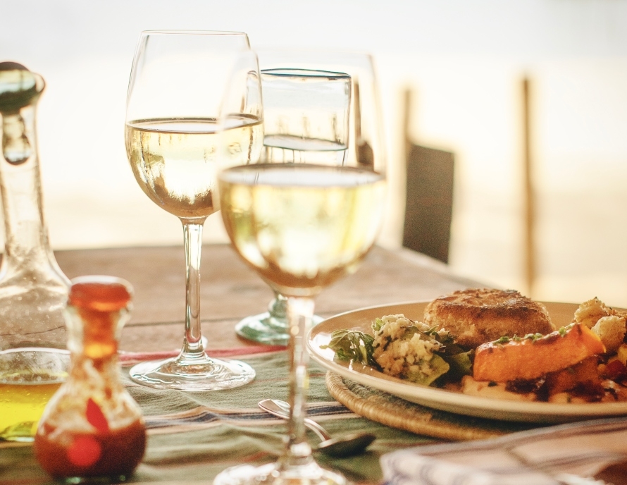 Elegant dining setup with wine glasses and a meal, backlit by warm sunlight.