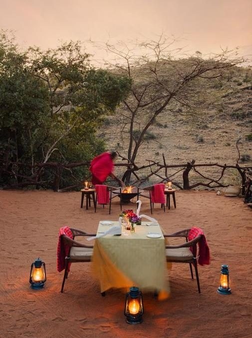 A private dining table set outdoors at dusk illuminated by lanterns and surrounded by nature.