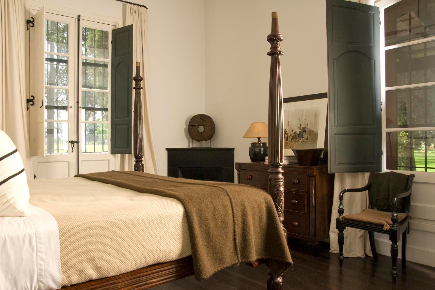 Elegant room with a four-poster bed, dark wood furniture, and open windows overlooking a lawn.