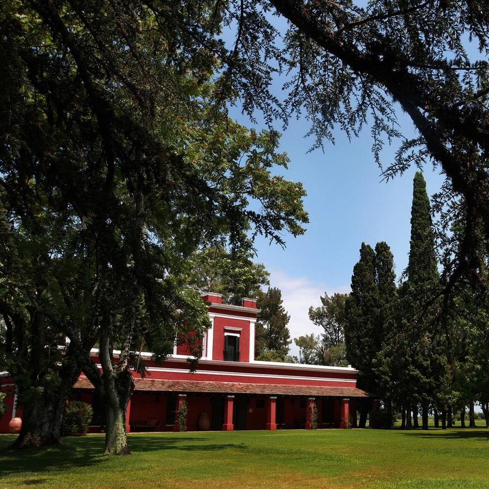 A red-roofed hacienda style building set amidst lush green trees and lawn under a clear blue sky.