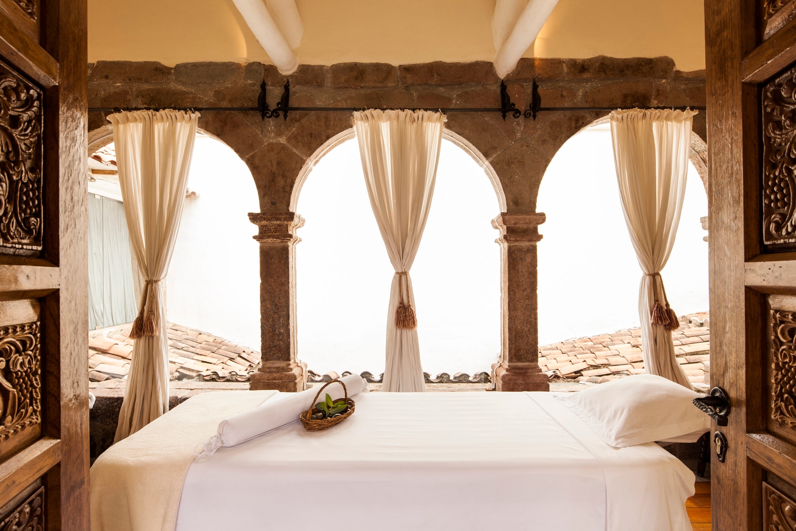 Rustic spa room with a massage table framed by arched stone doorways and draped curtains.