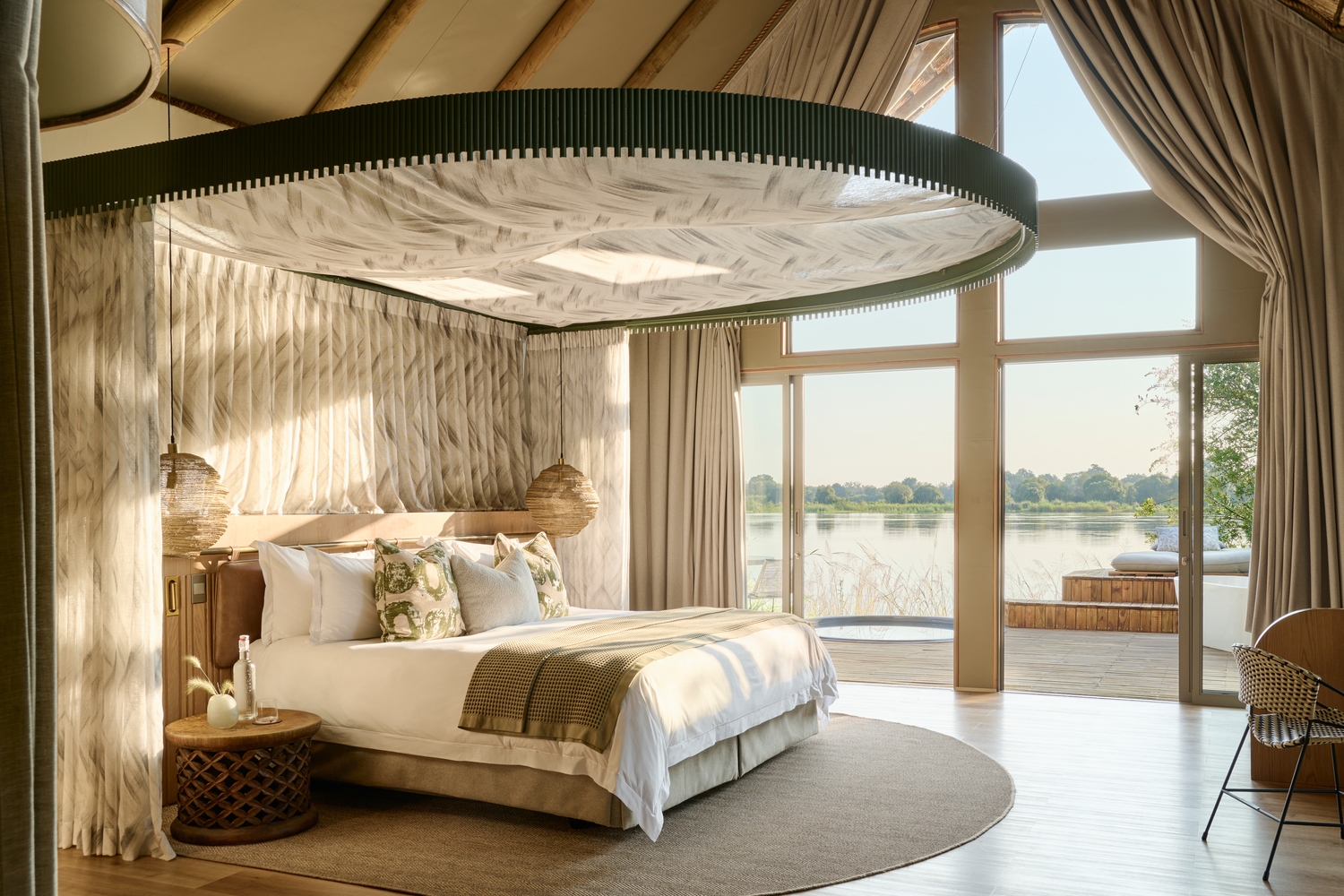 A modern luxury bedroom at Victoria Falls River Lodge with a view of the river through large glass sliding doors.