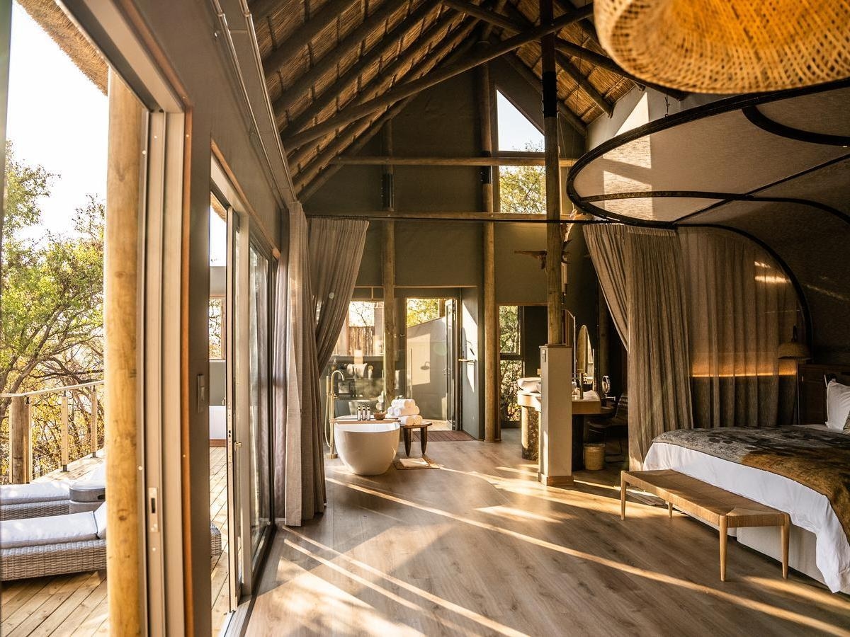 Interior of a safari suite with a white bathtub and large bed opening onto a deck at Victoria Falls River Lodge