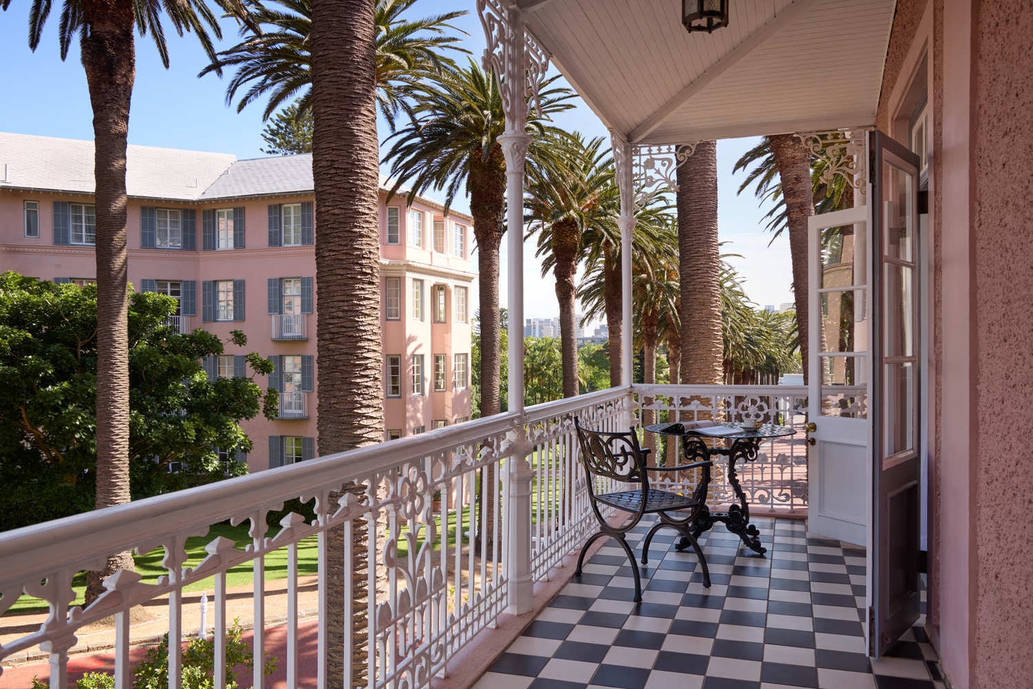 View from a Mount Nelson balcony showing checkered floors, ornate white railings, and tall palm trees.