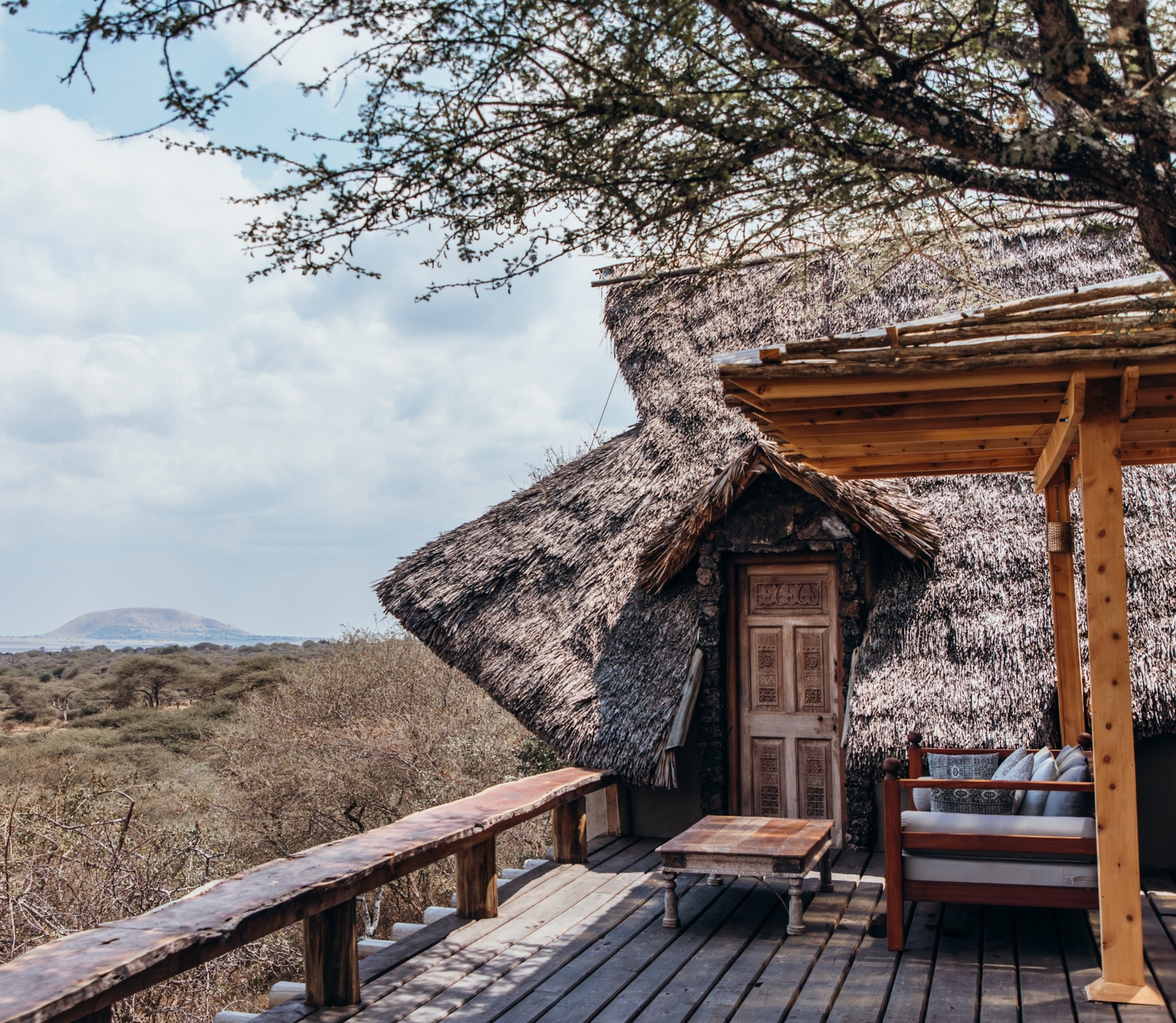 Exterior image of hotel roof terrace, with covered seating and a small wooden table, overlooking a view of wilderness bushland