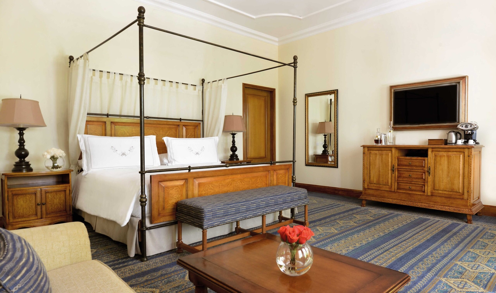 Elegant bedroom with a four-poster bed, wooden furniture, and a decorative blue carpet.