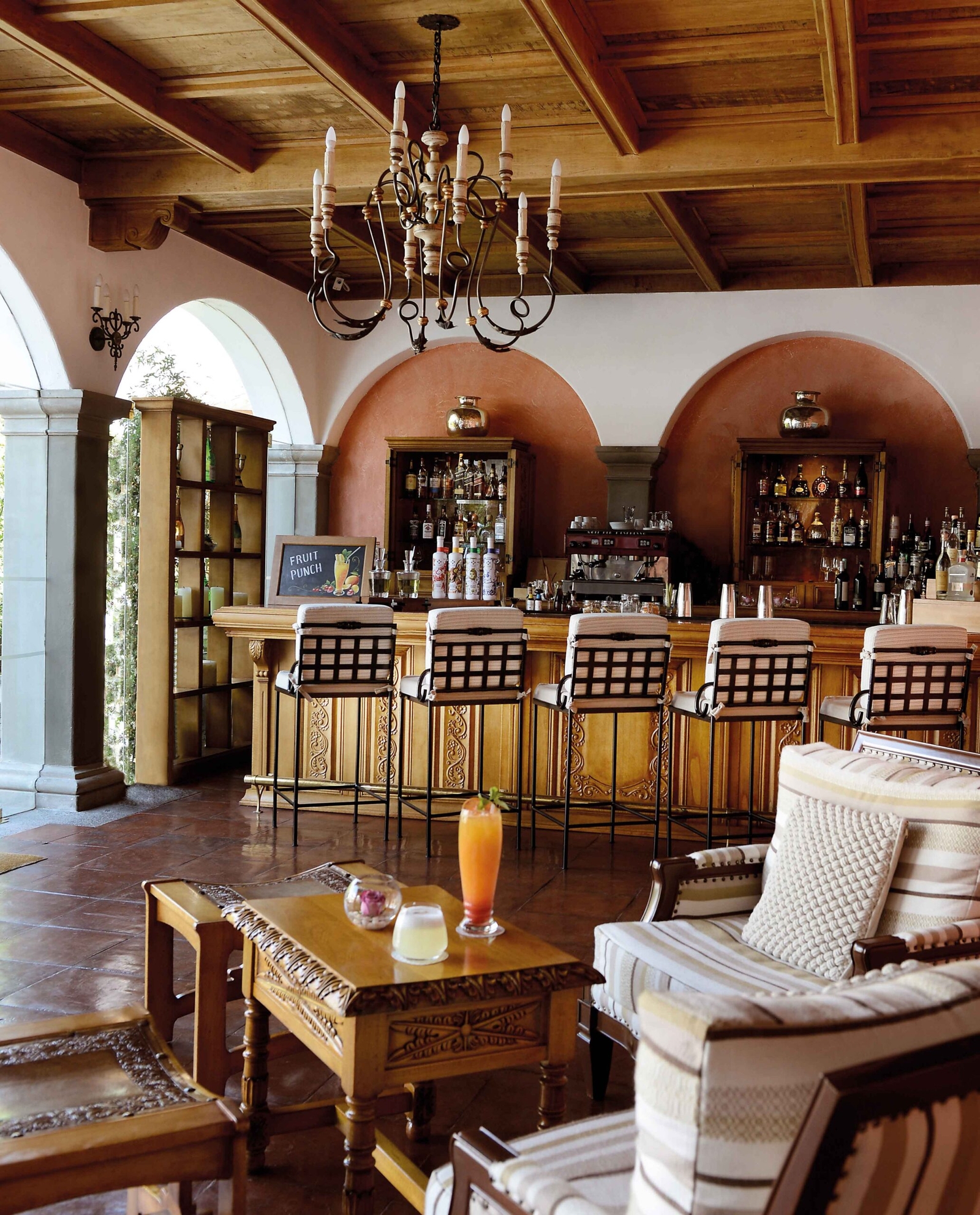 Elegant bar area with wooden stools, intricate chandeliers, and a terracotta arch.