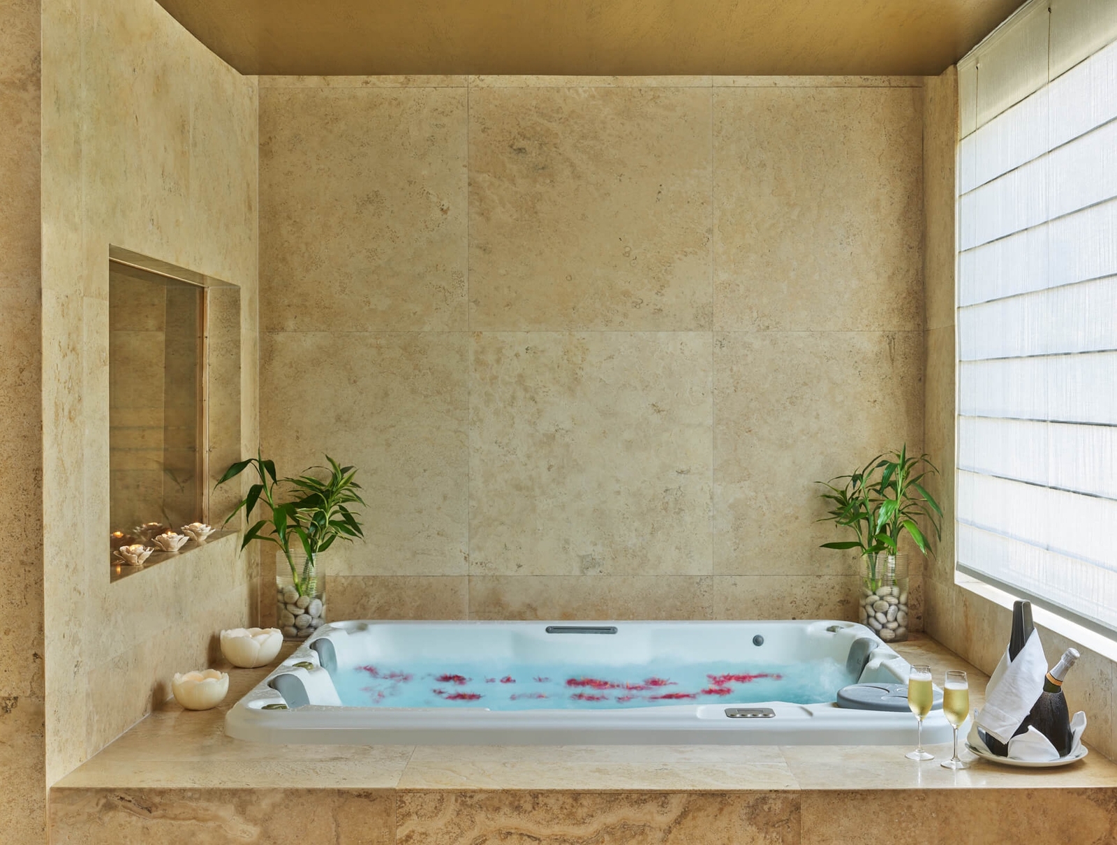 Luxurious bathtub with plants and champagne in a serene beige bathroom.