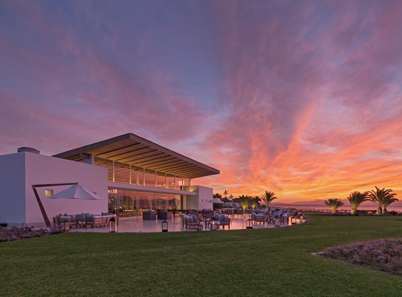 Modern beachfront building at sunset with vibrant sky and palm trees.