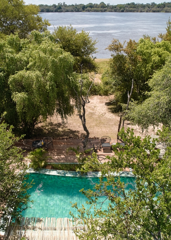 A green tiled plunge pool on a wooden deck surrounded by trees next to a large river at Victoria Falls River Lodge.