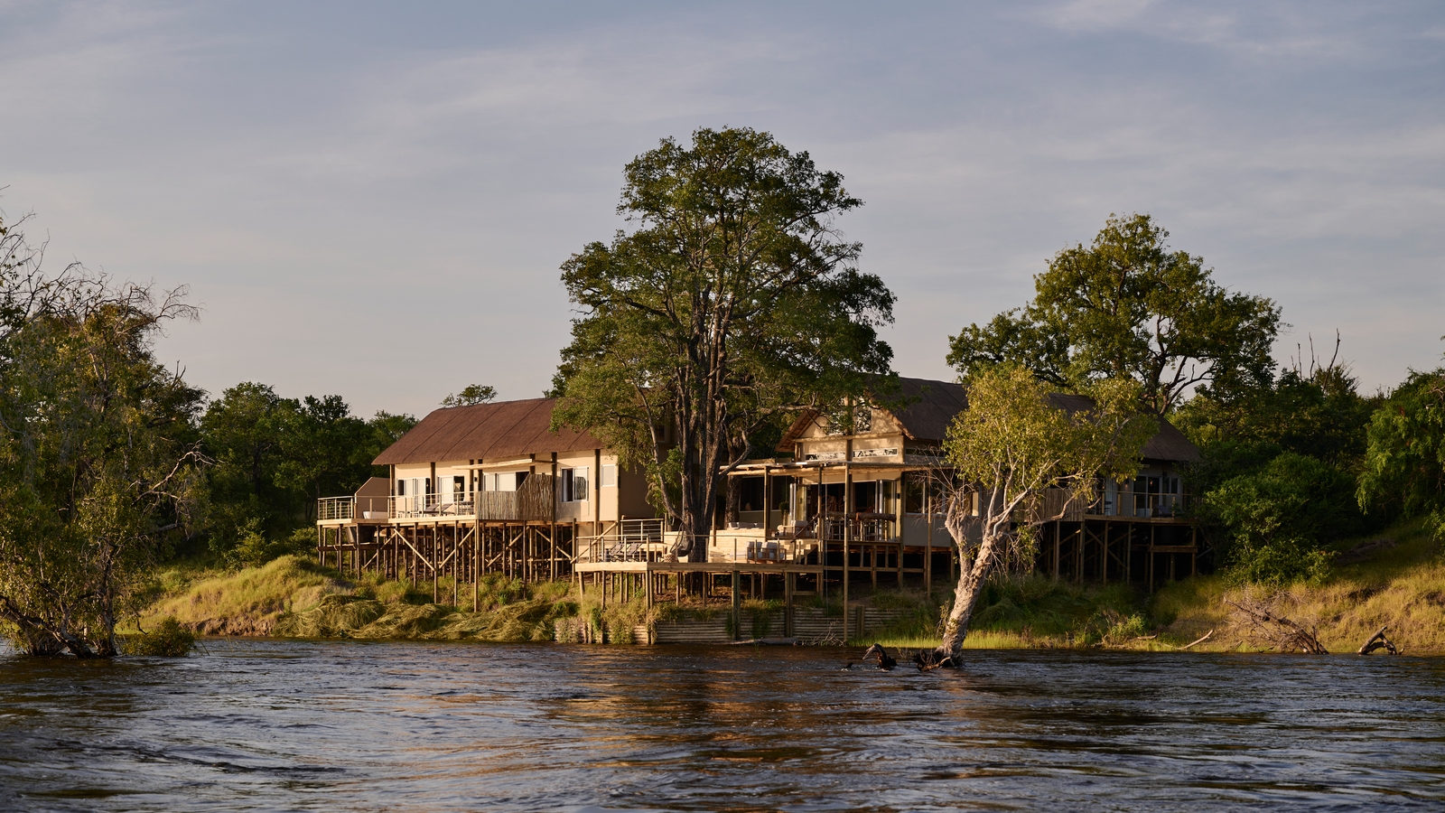 Exterior view of a waterfront villa on stilts at Victoria Falls River Lodge during the golden hour.