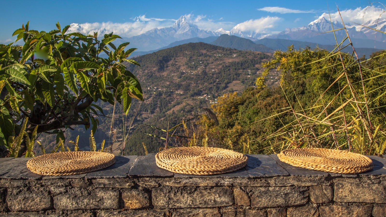 Three straw mats on a stone wall with a Himalayan mountain backdrop.