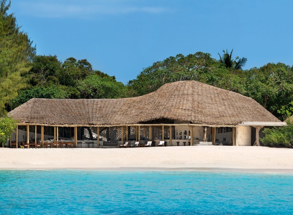 Thatched roof hut on the beach surrounded by greenery with turquoise water in front at Mnemba Island in Zanzibar