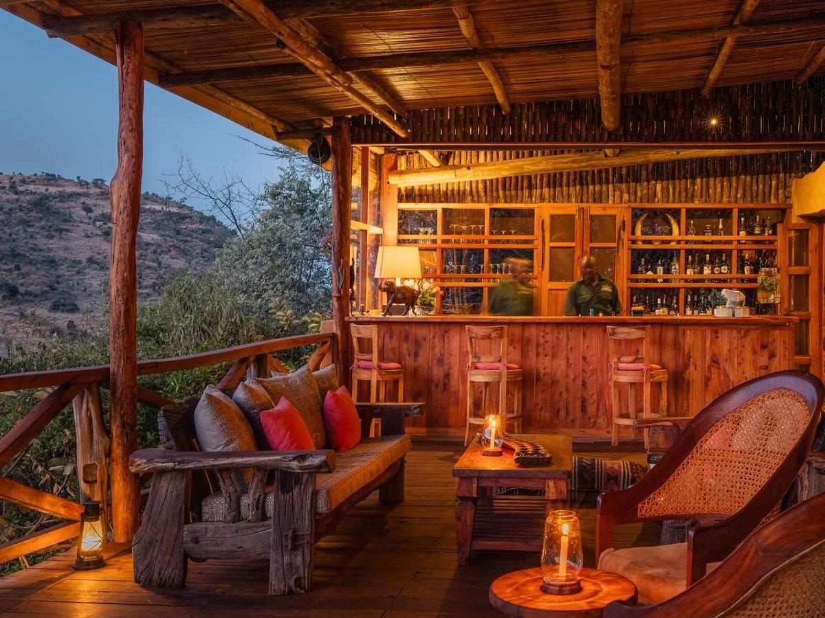 A cozy, warmly lit open-air wooden bar lounge overlooking natural scenery in the evening.