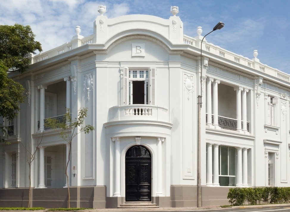 A white two-story historic building with classical columns and balconies under a blue sky at Hotel B in Lima, Peru.