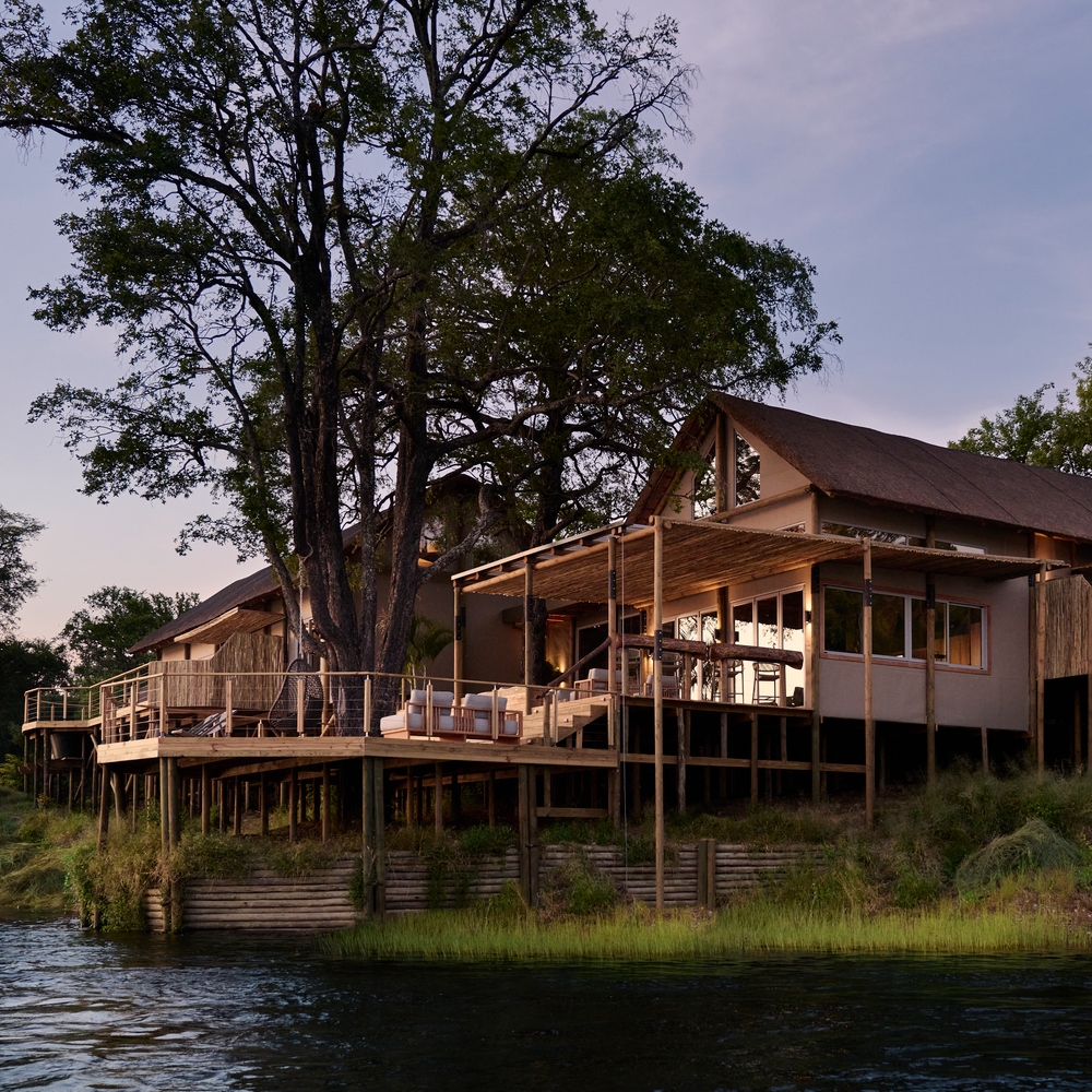 A large stilted luxury villa at Victoria Falls River Lodge with expansive wooden decks situated along the riverbank.