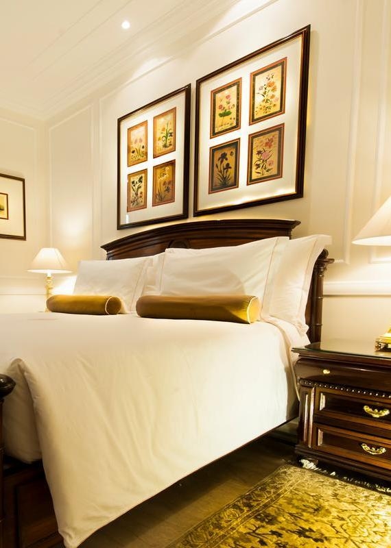 A luxury bed with white bedding and gold pillows positioned under two large framed floral pictures in a Heritage Suite.
