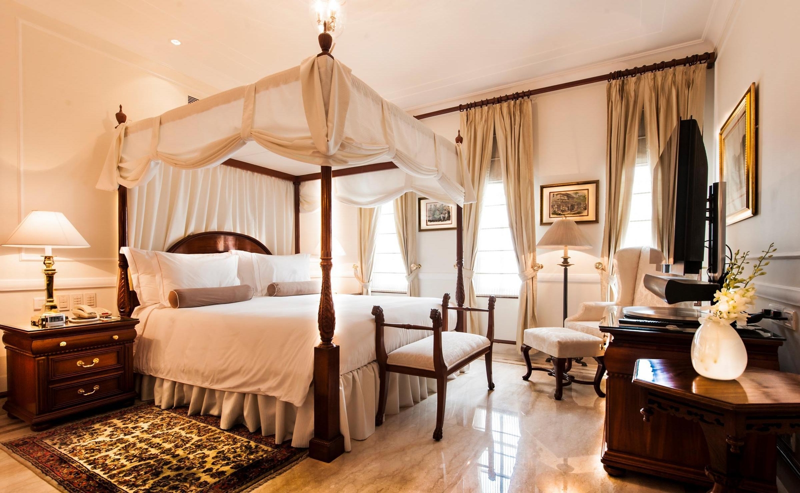 A bedroom featuring a white draped four-poster bed, marble floors, and elegant curtains in a Luxury Suite.