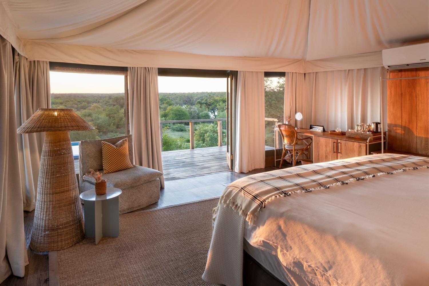 A luxury tented bedroom at Simbavati Hilltop Lodge with warm sunset light and a view of the wilderness.
