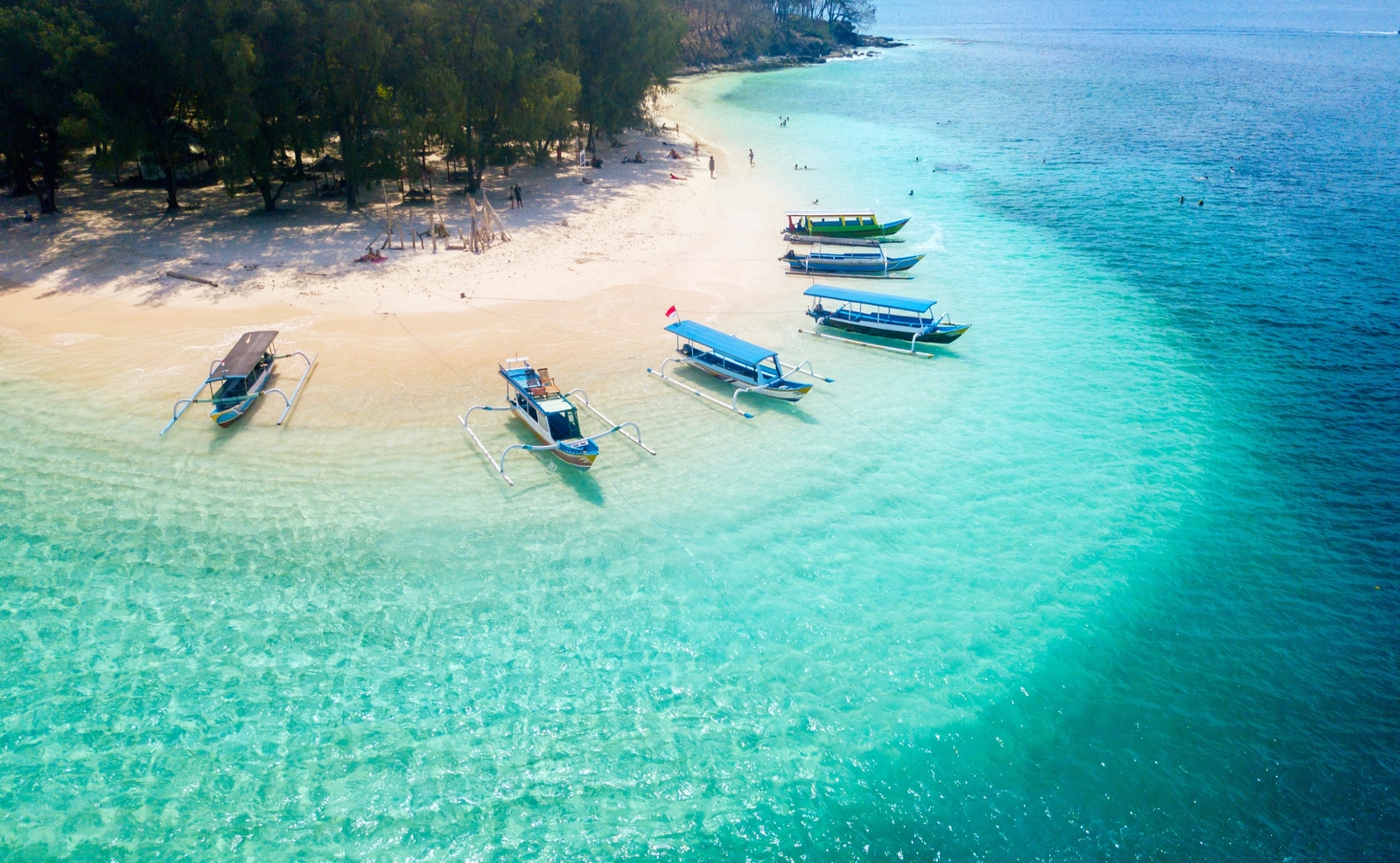 Aerial view of turquoise ocean water and a white sand beach with several small boats anchored near the shore.