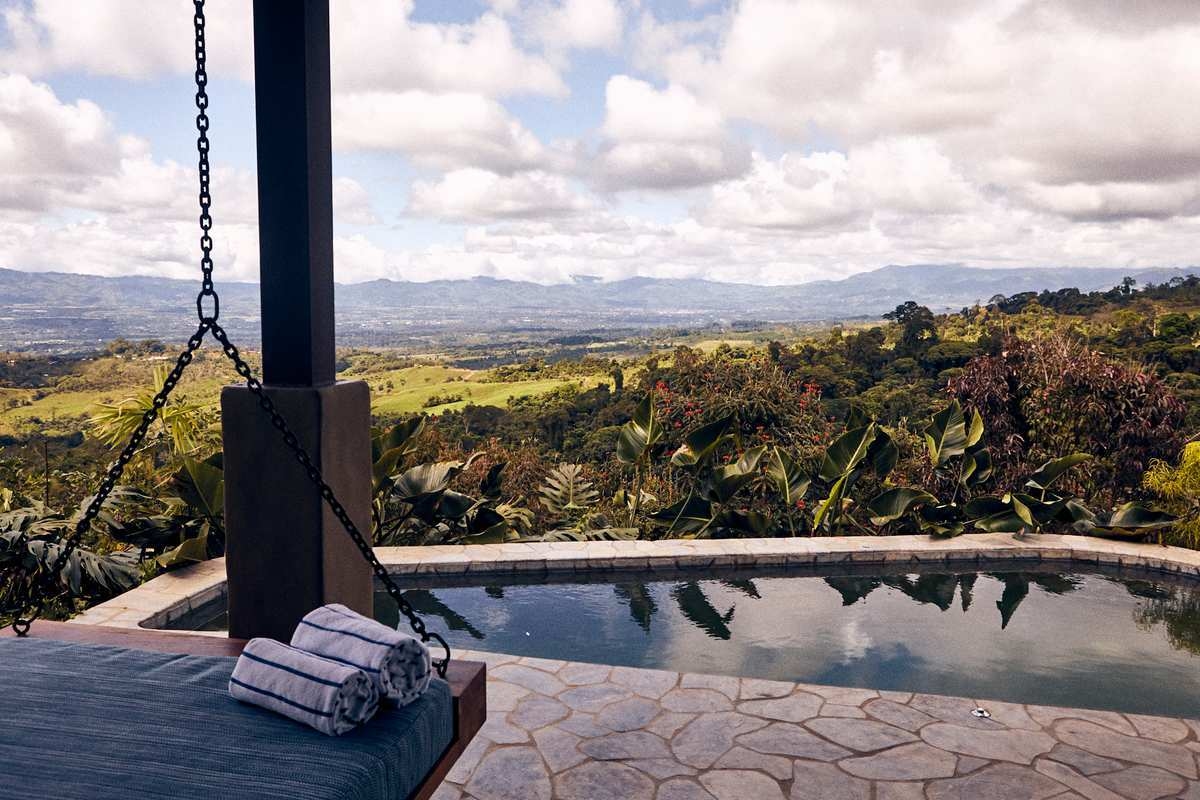 A hanging daybed on a stone terrace overlooking a private infinity pool and wide mountain valley views.
