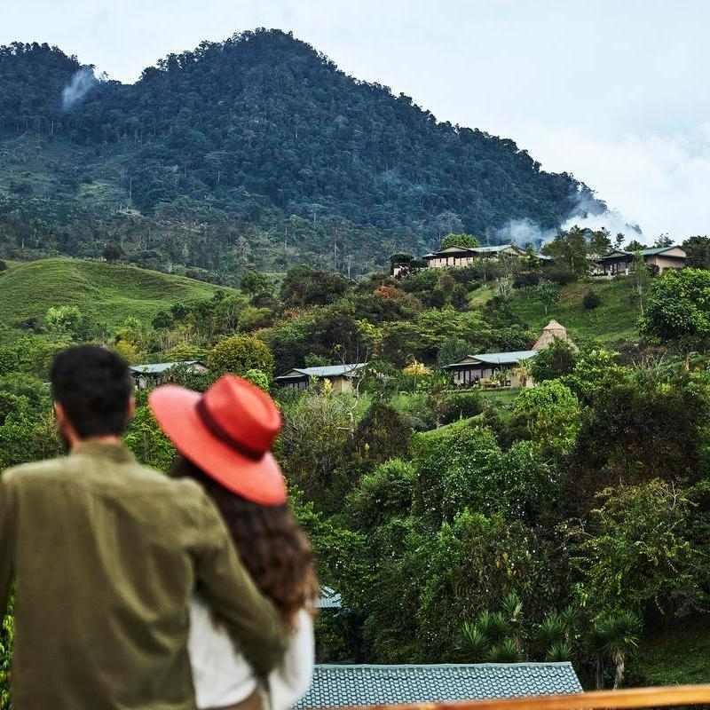 The back of two people looking toward a forested mountain and Hacienda AltaGracia's casitas tucked among the trees.