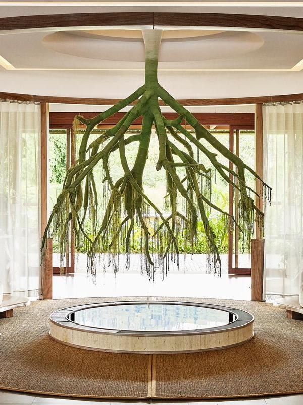A large green tree root sculpture suspended over a circular pool in a serene, modern spa room with wooden accents.
