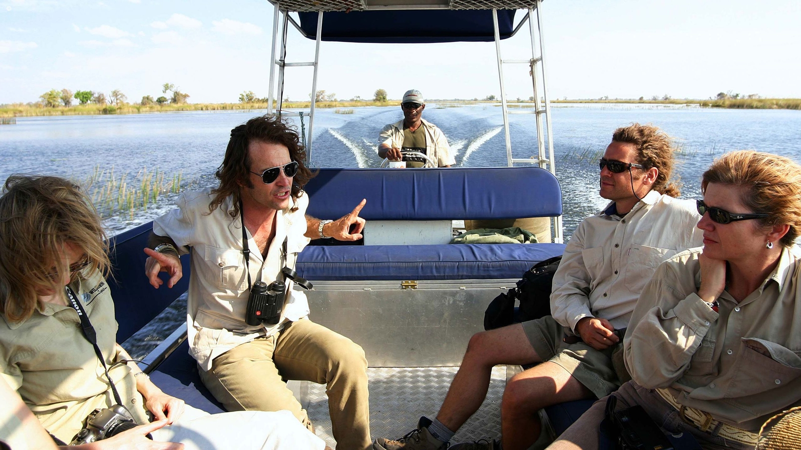 A guide driving a motor-powered boat through a delta with four passengers sitting in front in mid-conversation