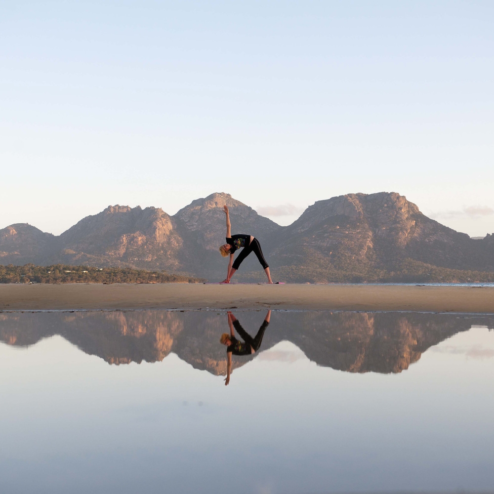 A woman doing yoga reflected in the sea at Muirs Beach near Saffire Freycinet