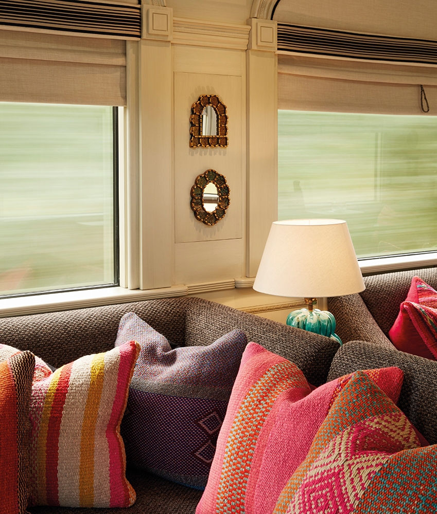 Close-up of colorful patterned pillows on a sofa inside a luxury train with large windows.