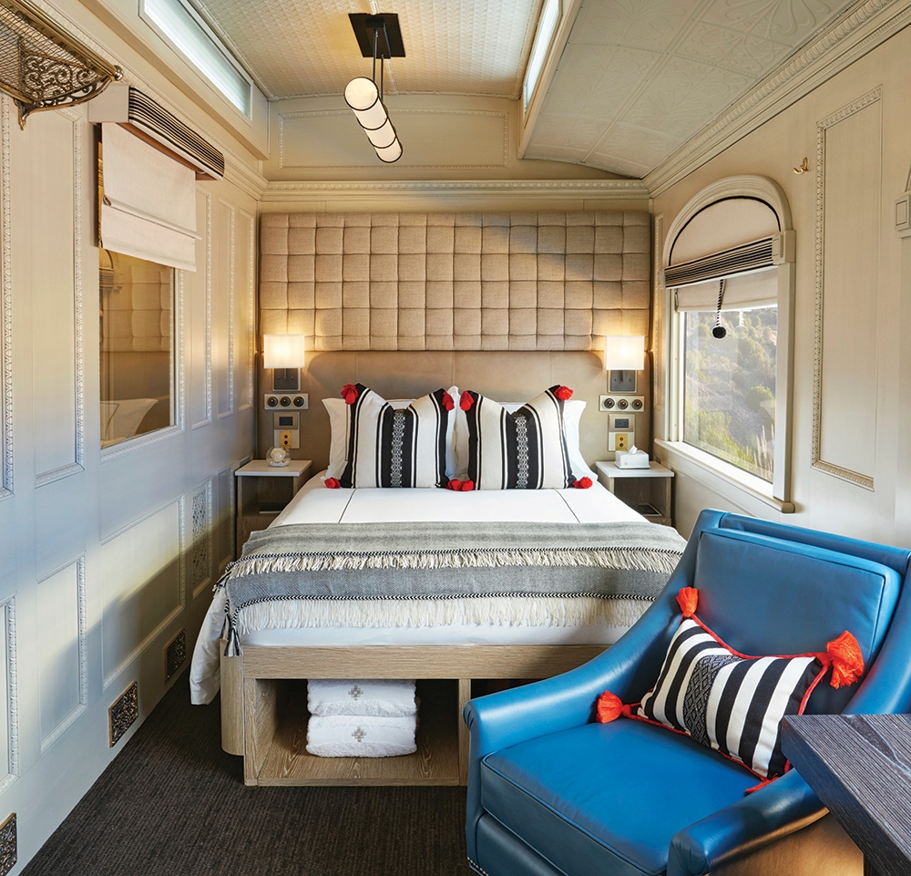 A luxury train bedroom suite with a double bed, blue leather chair, and elegant wall paneling.
