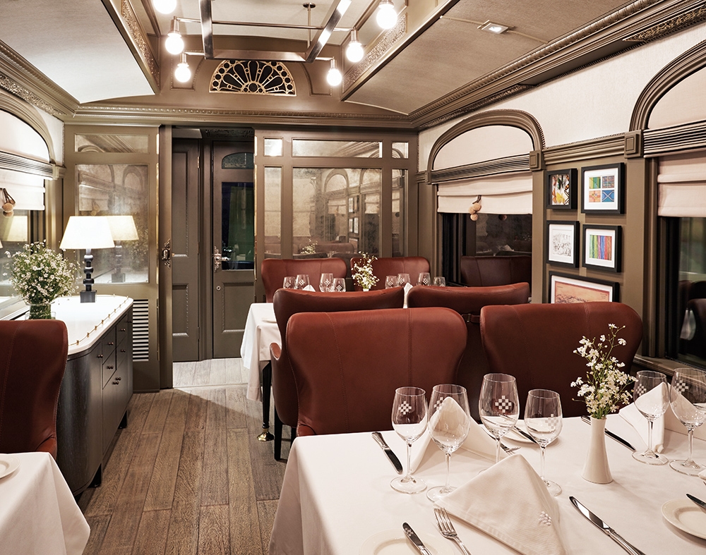 Interior of a luxury train dining car with set tables, leather chairs, and warm ambient lighting.