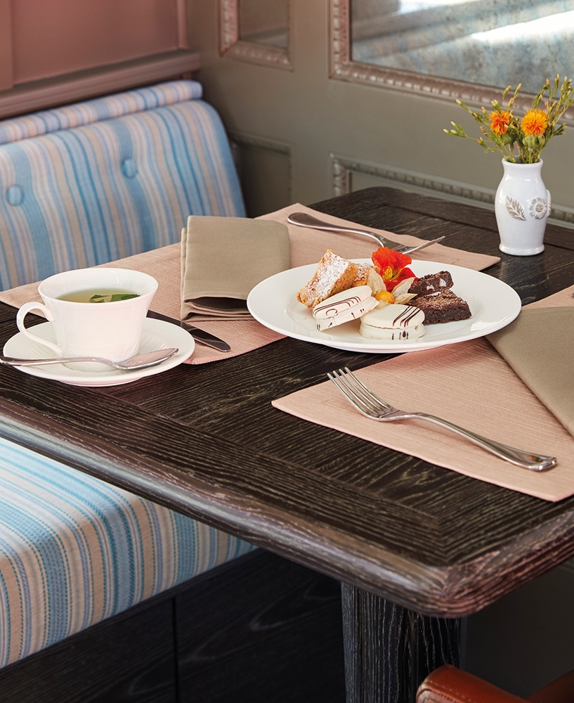Afternoon tea service on a train featuring a white tea cup and a plate of cakes and brownies.