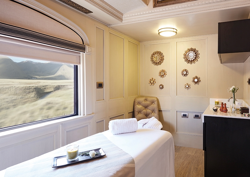A white massage table inside a bright, luxury train spa room with decorative wall mirrors.