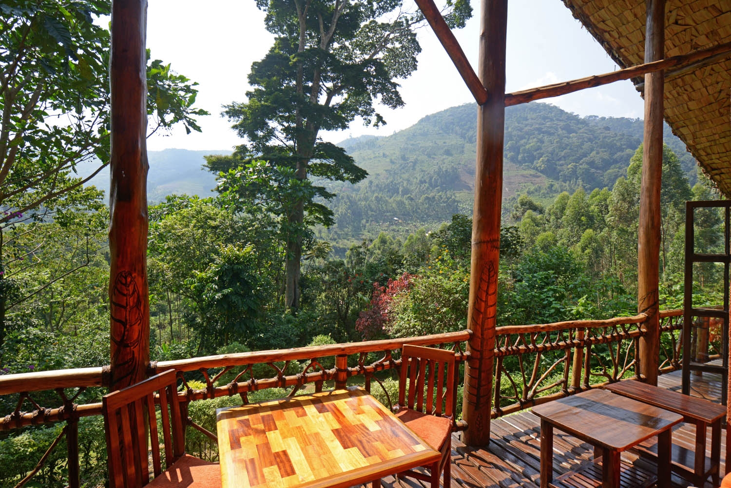 Server bringing food to a couple on a wooden balcony facing a forested valley at Mahogany Springs uganda.