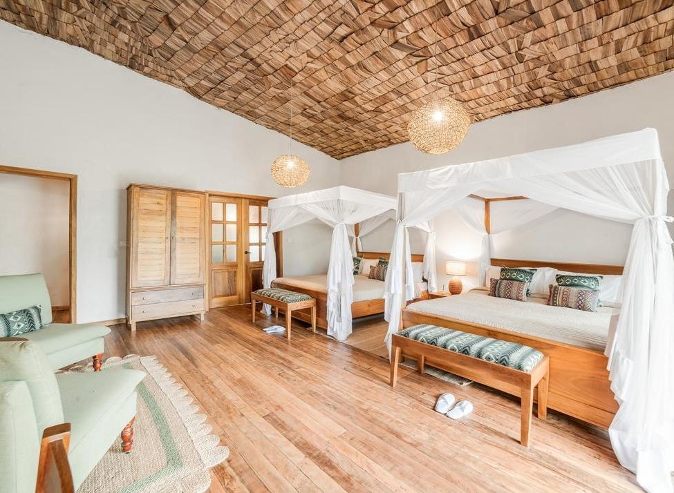 Bedroom at Mahogany Springs uganda with two canopy beds, white netting, wooden floor, and a woven ceiling.