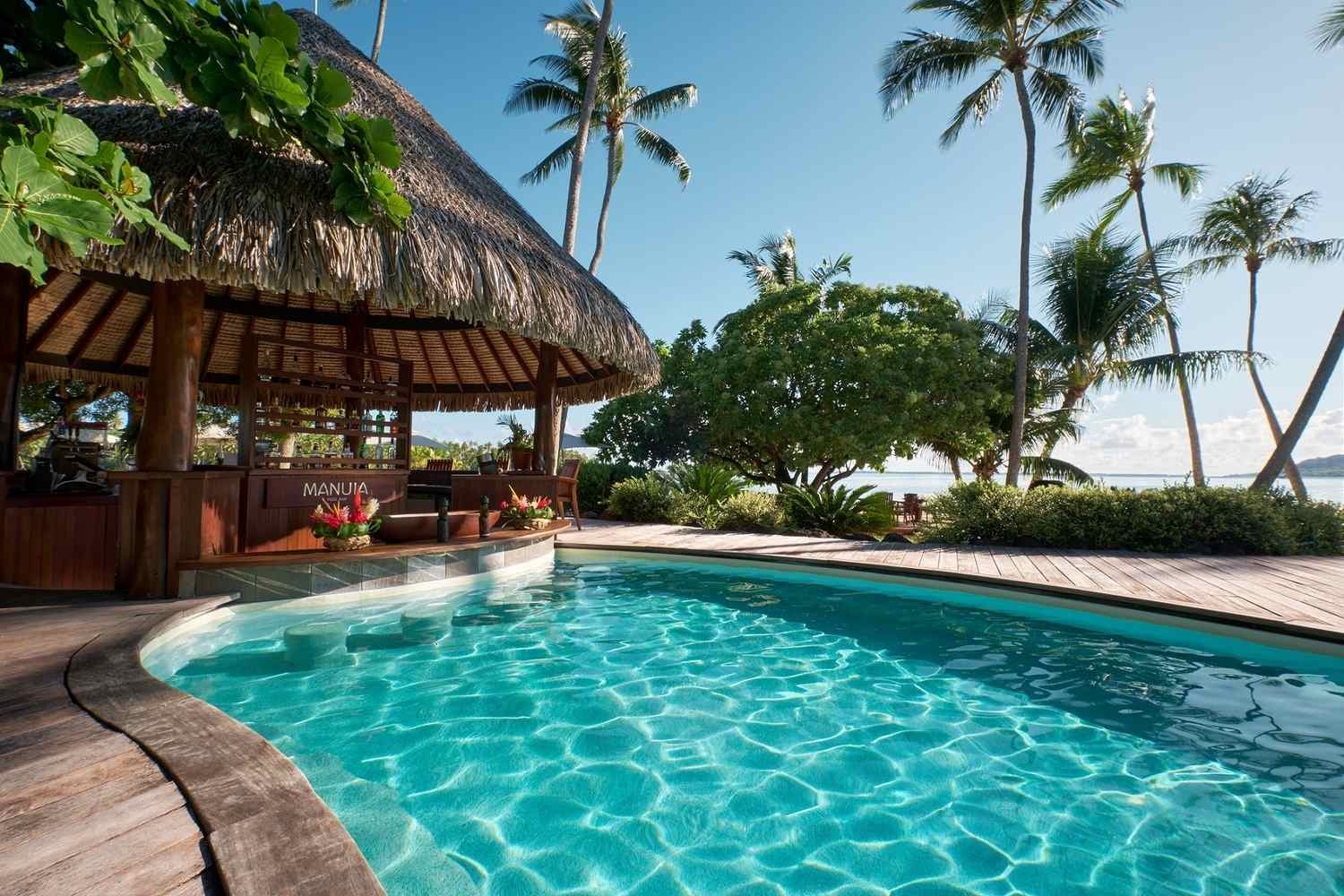 Swim-up bar with a thatched roof and barstools next to a swimming pool at Le Taha'a by Pearl Resorts in French Polynesia.