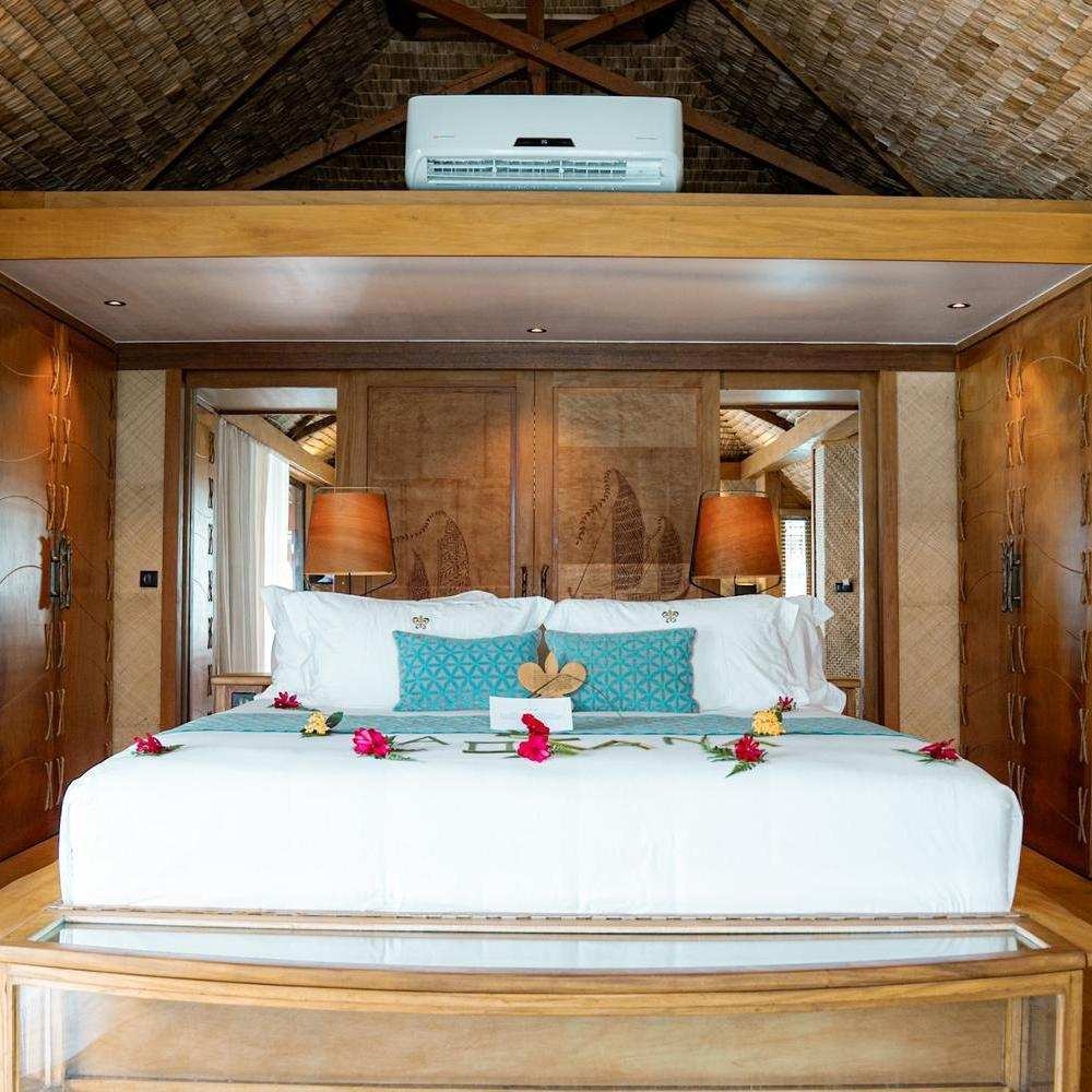 Bed decorated with floral arrangements inside an overwater bungalow bedroom at Le Taha'a by Pearl Resorts in French Polynesia.