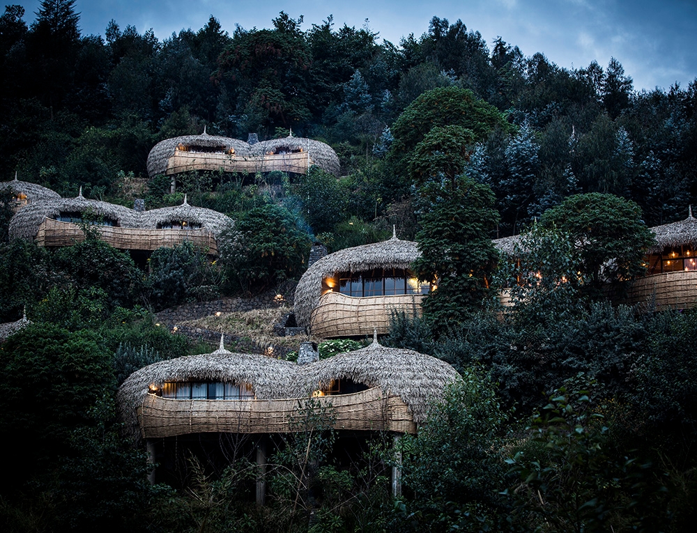 A hillside view of thatched-roof villas tucked away in thick green forest under a clear sky.