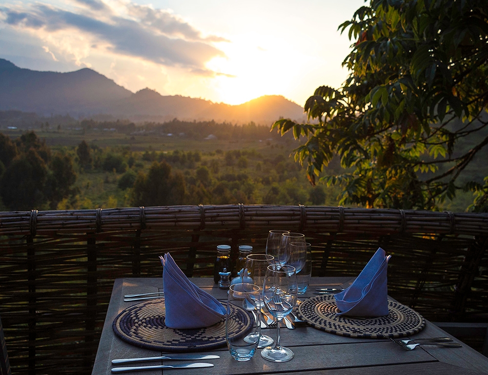 A formal dinner table setting on a wooden deck overlooking a mountain valley during a golden sunset.
