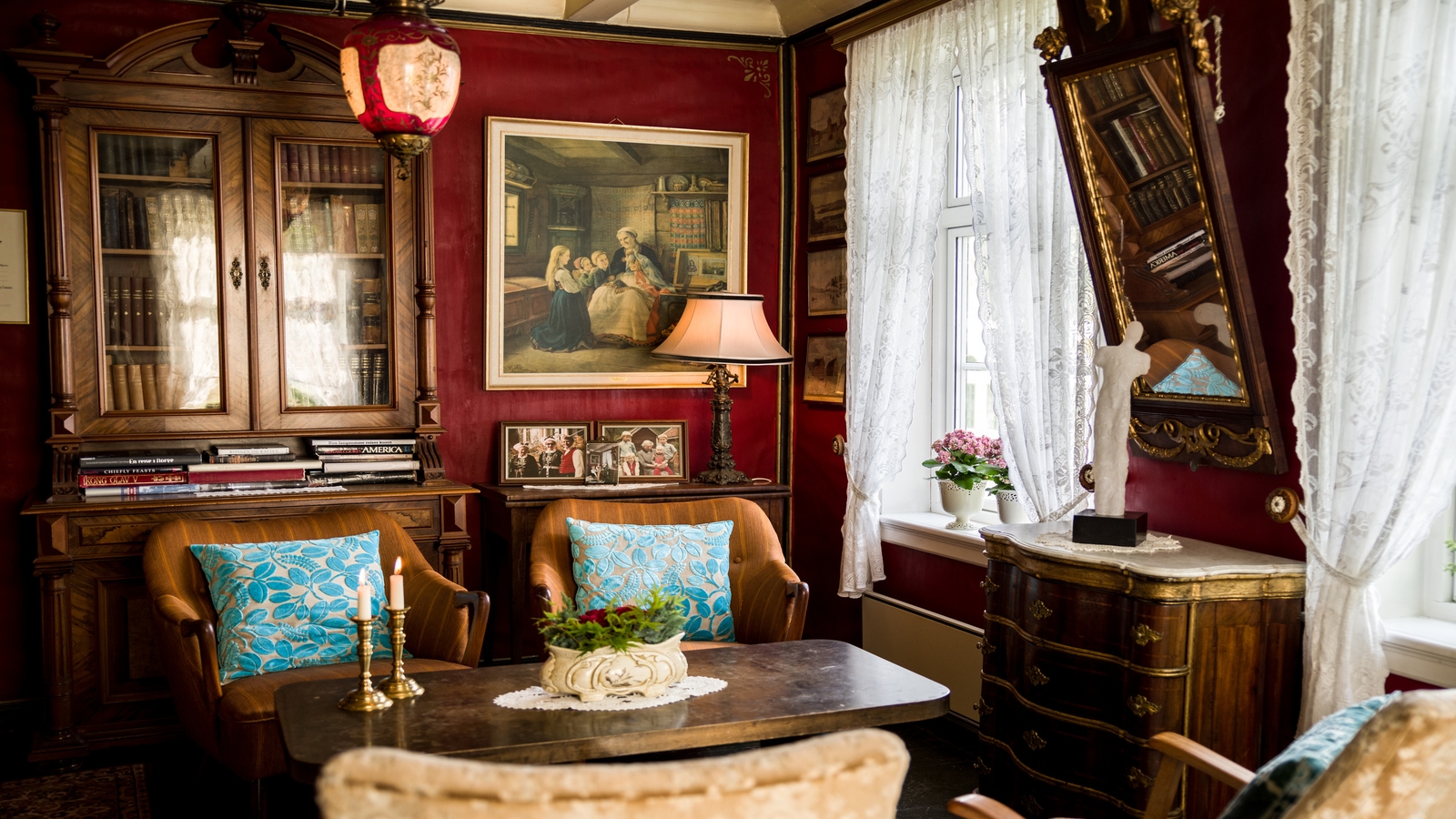 Elegant vintage room with rich red walls, ornate furniture, and lace curtains.
