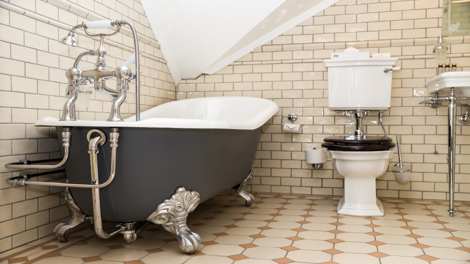 Vintage bathroom with claw-foot tub, toilet, and sink, tiled floor and walls.